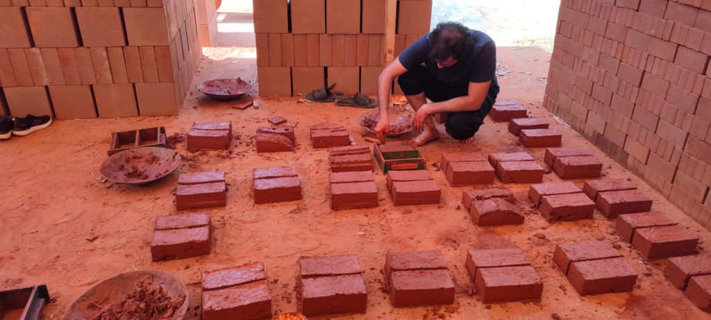A person making bricks made of mud which are along many other bricks.