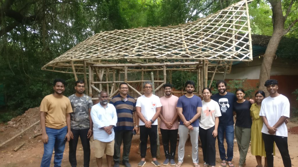 People standing for a photo in front of bamboo house.