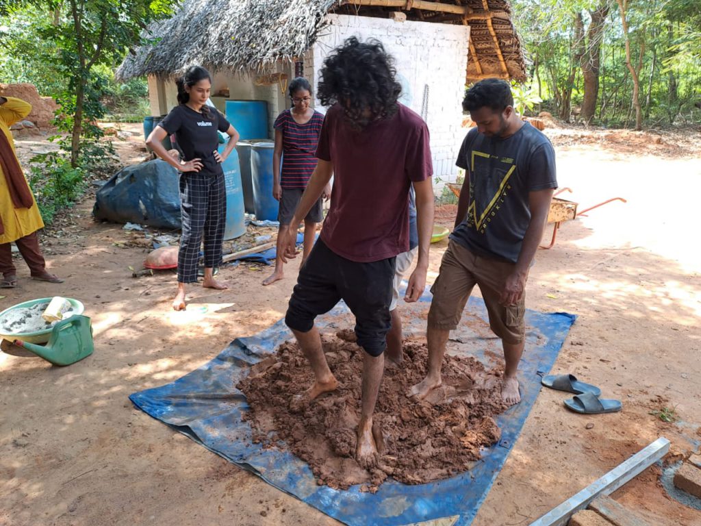 Two boys mixing mud, hay and water. Two girls watching them mix it.