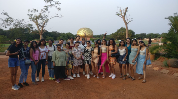 Girls standing in front of a golden globe surrounded by a garden.